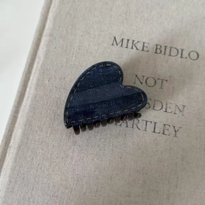 Detail of heart-shaped hair claw clip with dark denim texture and yellow stitching