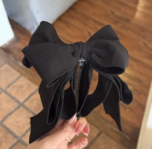 Detail of a matte black layered bow hair clip with long tassels and fabric texture