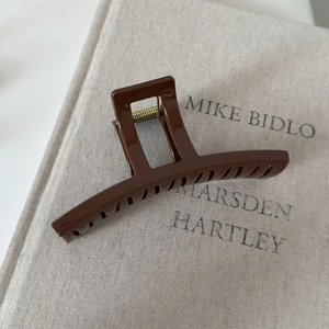 Macro detail of glossy brown hair claw clip with golden metal spring on minimalist book