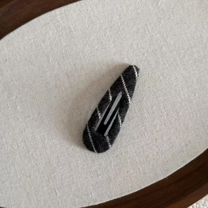 Close-up of a black knit striped BB hair clip with wool texture on a beige fabric background