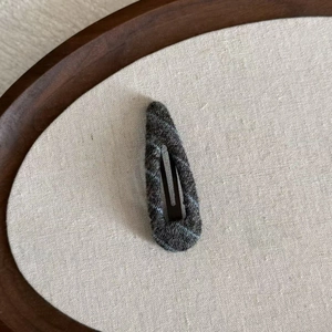 Detailed close-up of dark grey checkered wool knit snap hair clip on a neutral fabric