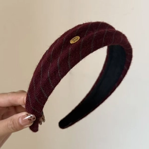 Detail of burgundy knitted headband showing thick texture and golden handmade metal tag