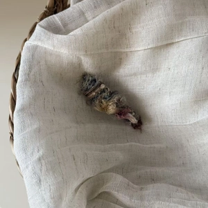 Detail of handcrafted grey and purple plush knit hair clip on textured white linen surface