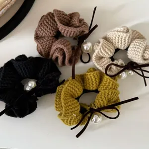 Detailed view of four knitted hair scrunchies with pearls and bows in assorted colors