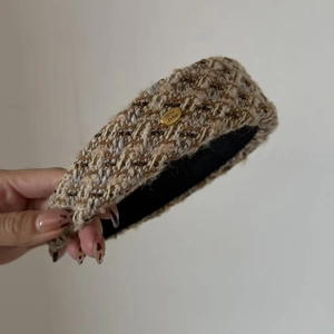 Close-up of French tweed headband featuring textured beige fabric and gold metal logo