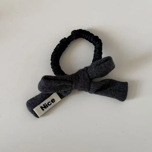 Detail of a grey wool bow hair tie with Nice label on a black scrunchie elastic