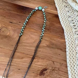 Detail of bohemian braided necklace with green beads and silver leaf pendant on wood