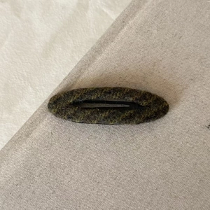 Vintage green tweed knit hair clip with striped texture on soft gray linen background