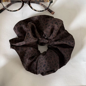 Brown leopard print satin scrunchie with elastic design paired with glasses on white fabric