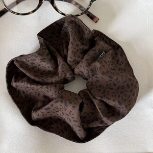 Detailed macro view of a leopard print satin scrunchie with fashion label on white fabric