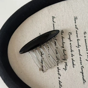Close-up of handmade black hair comb with gold logo and silver metal teeth on fabric