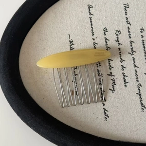 Macro detail of amber resin hair comb showing the silver metal teeth and engraved text
