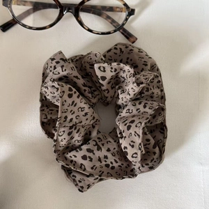 Leopard print satin scrunchie styled with glasses on textured fabric background