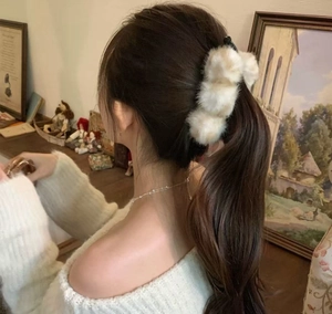 Détail d'une pince à cheveux en peluche beige sur une coiffure en queue de cheval