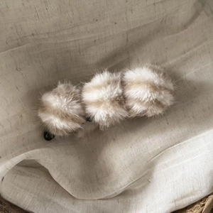 Détail d'une pince à cheveux en peluche avec pompons rayés sur tissu en lin