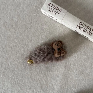 Close-up of fluffy gray faux fur bow hair clip with brown flocked bear and gold handmade tag
