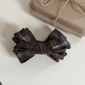 Detail of multi-layered plaid bow hair clip with textured fabric on a white background