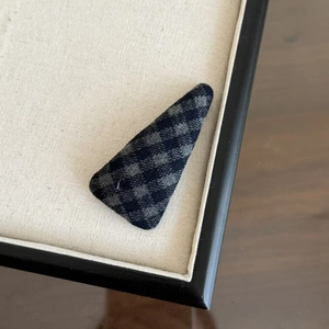 Pince à cheveux triangulaire à carreaux bleu foncé sur un plateau à bijoux en tissu beige