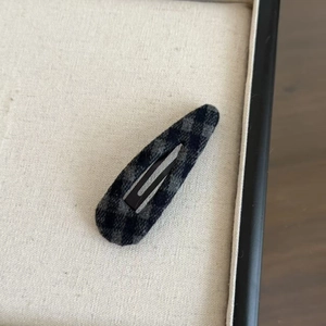 Gros plan d'une barrette à carreaux gris et noirs posée sur un plateau à bijoux beige