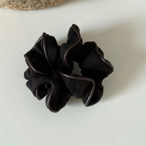 Close-up of black striped knit scrunchie with brown leather trim edge on white surface