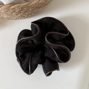 Close-up of black knit scrunchie with brown faux leather trim and cozy home background