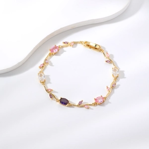 Detail eines vergoldeten Rankenarmbands mit rosa und lila Zirkonsteinen auf weißem Hintergrund