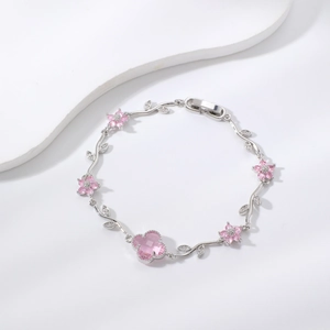 Silbernes Armband mit rosa Zirkonia-Blumen und funkelnden Weinblättern auf weißem Steinhintergrund