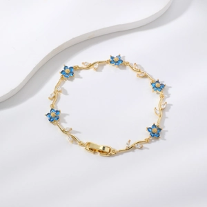 Elegante pulsera dorada con pétalos azules y detalles de hojas en circonita brillante