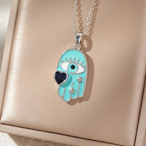 Macro shot of silver Hamsa necklace with teal enamel, blue heart gem and star details