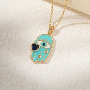 Golden Hamsa Hand necklace with blue evil eye heart pendant on white stone surface