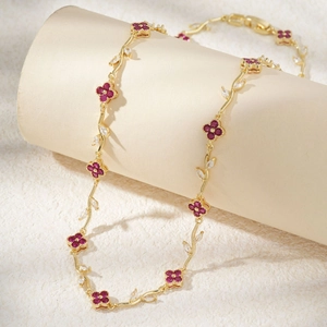 Elegant gold vine necklace with red four-petal clover flowers and crystal leaf accents