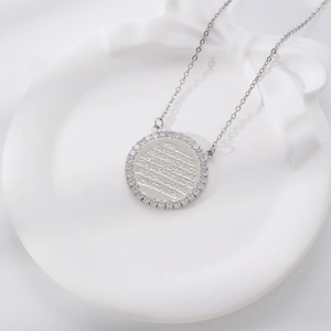 Silver round pendant necklace with Arabic script and zircon ring on white ceramic plate