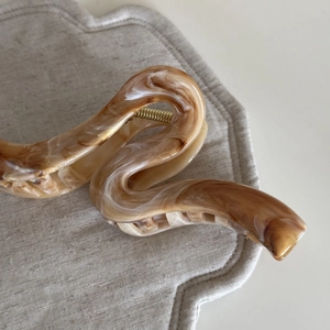 Detail view of brown amber marble hair claw clip with golden spring on grey fabric