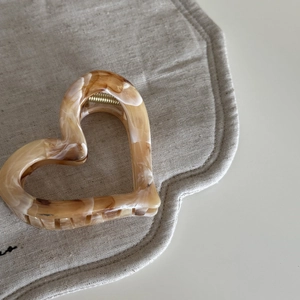Macro shot of heart-shaped acetate hair claw with amber marble pattern and gold spring