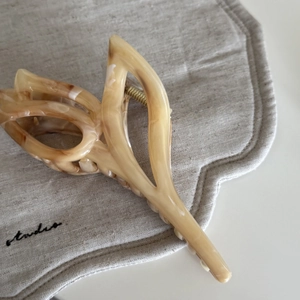 Macro shot of marble textured brown hair claw clip with golden metal spring on linen fabric