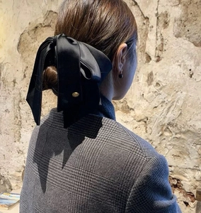 Detail of elegant black satin ribbon bow hair claw with gold logo charm on model