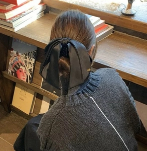 Close-up of a large black bow hair claw clip styled on long hair in a library setting
