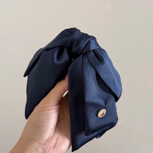 Elegant navy blue satin bow headband with gold metallic tag and knotted silk texture