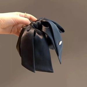 Detail view of large black satin bow hair claw clip with a premium silk luster and gold logo