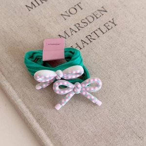 Detail of two green elastic hair ties with pink checkered bows on a display card