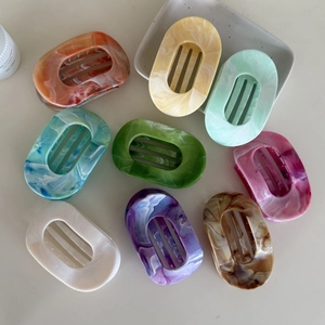 Flat oval marble hair claws in nine assorted colors displayed on a ceramic tray