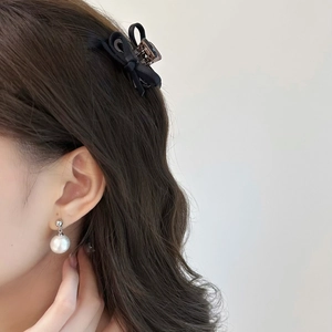 Gros plan d'une pince à cheveux à nœud noir et d'une boucle d'oreille en perle sur modèle
