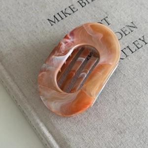 Detailed close-up of oval cut-out hair claw clip with amber marble texture finish