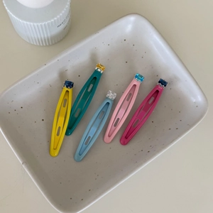 Set of five colorful sugar-shaped metal BB hair clips with gemstones on a ceramic tray
