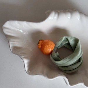 Close-up of cute orange fruit hair tie on white plate with green elastic band detail