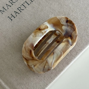 Detail view of oval flat hair claw with marble amber texture on minimalist background