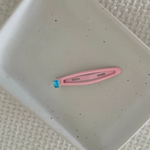 Close-up of a pink metal drop hair clip with a blue rectangular gemstone on a ceramic tray
