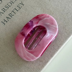 Detailed top view of a pink and white marble texture oval hair claw on a textured book