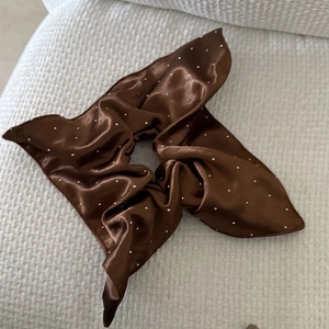 Close-up of brown satin bow scrunchie with sparkling rhinestones on textured white background