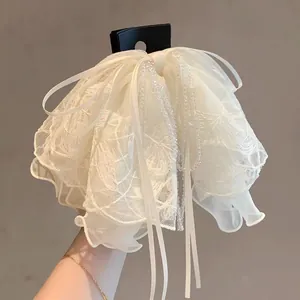 Détails d'une pince à cheveux élégante en dentelle blanche avec cristaux et rubans pendants